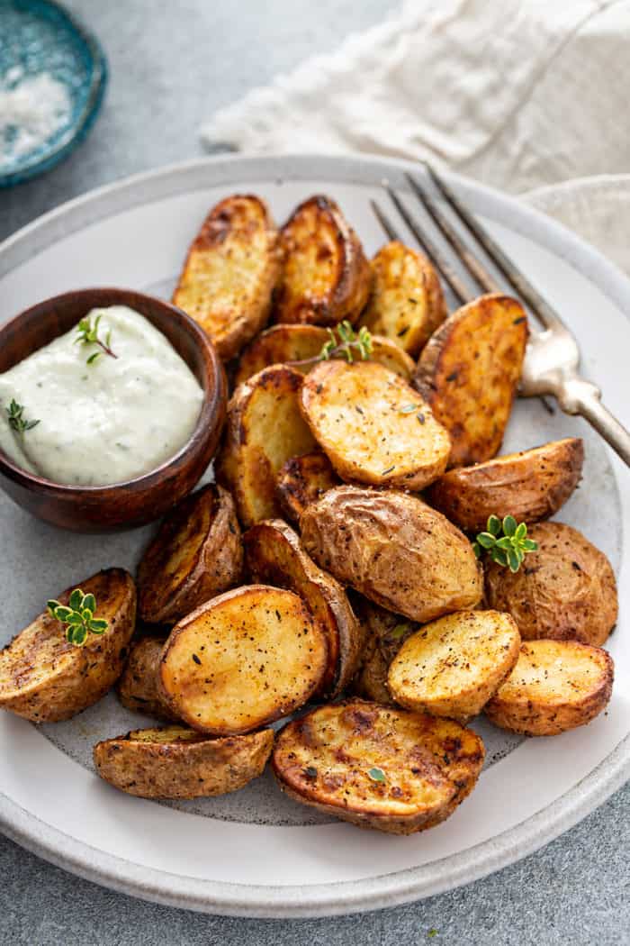 Air fryer roasted potatoes next to a ramekin of aioli and a fork on a white plate