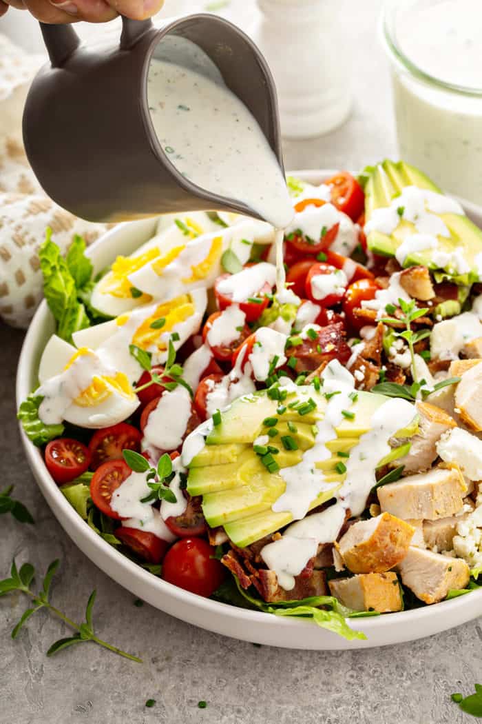 Ranch dressing being poured over the top of a cobb salad