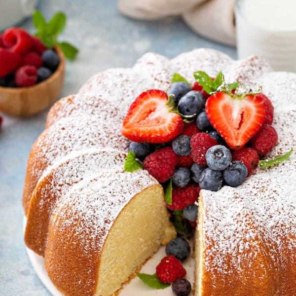 Sliced whipping cream cake on a white cake plate, garnished with fresh berries and powdered sugar