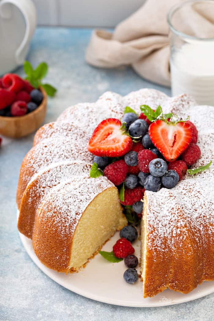 Sliced whipping cream cake on a white cake plate, garnished with fresh berries and powdered sugar