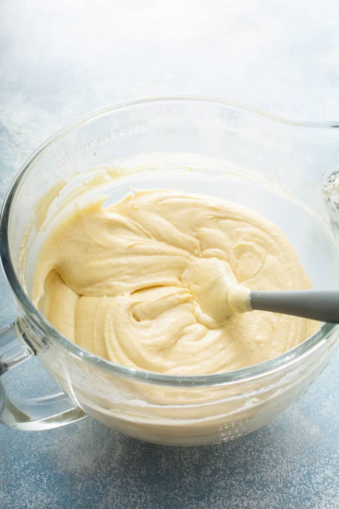 Whipping cream cake batter in a glass mixing bowl, being stirred with a spatula