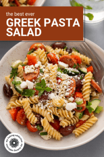 Close up view of greek pasta salad in a white bowl. Text overlay includes recipe name.