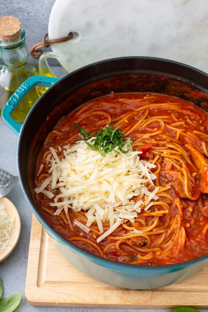 Cheese and basil being added to a pot of one-pot spaghetti