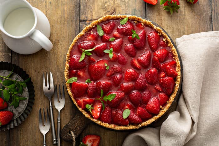 Overhead view of assembled fresh strawberry pie on a wooden table, surrounded by forks and napkins