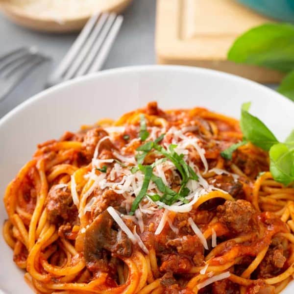 Serving of one-pot spaghetti in a white pasta bowl, garnished with cheese and basil