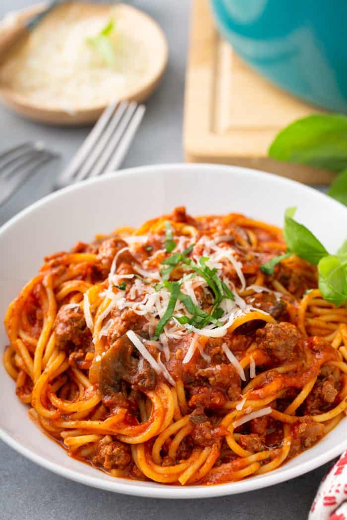 Serving of one-pot spaghetti in a white pasta bowl, garnished with cheese and basil