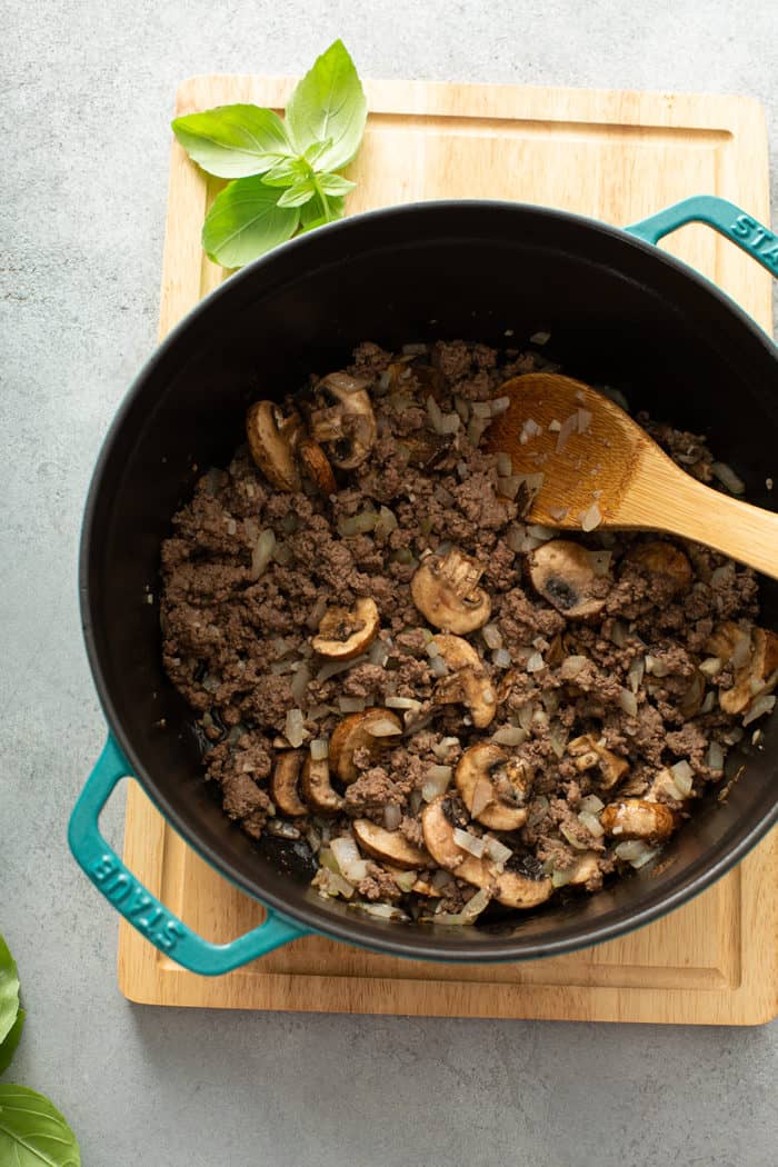 Spoon stirring browned meat and mushrooms in a large dutch oven