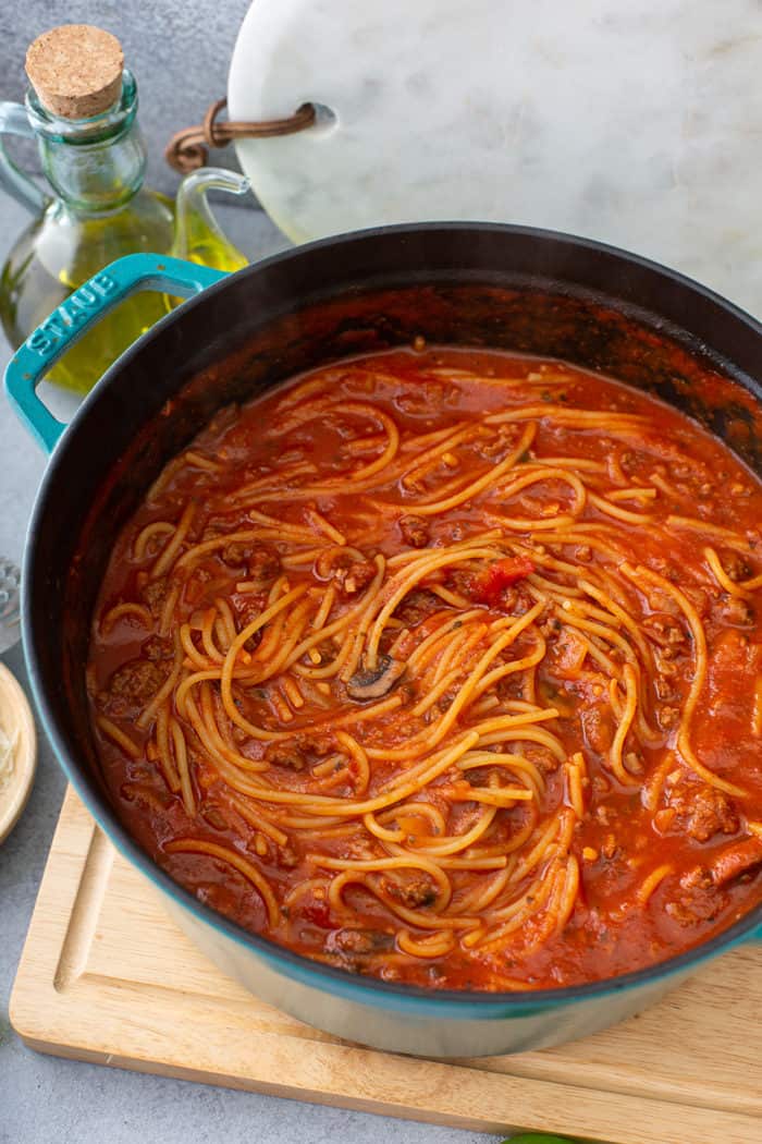 One-pot spaghetti in a large dutch oven, set on a wooden cutting board