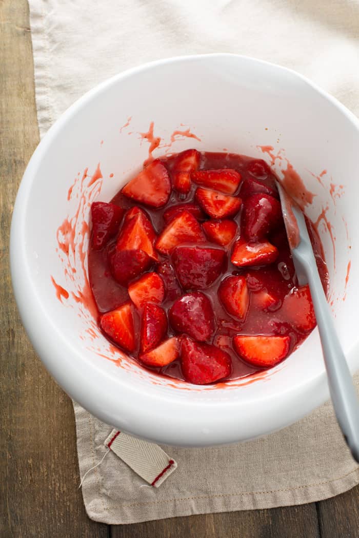Spatula stirring together fresh strawberry pie filling in a white mixing bowl