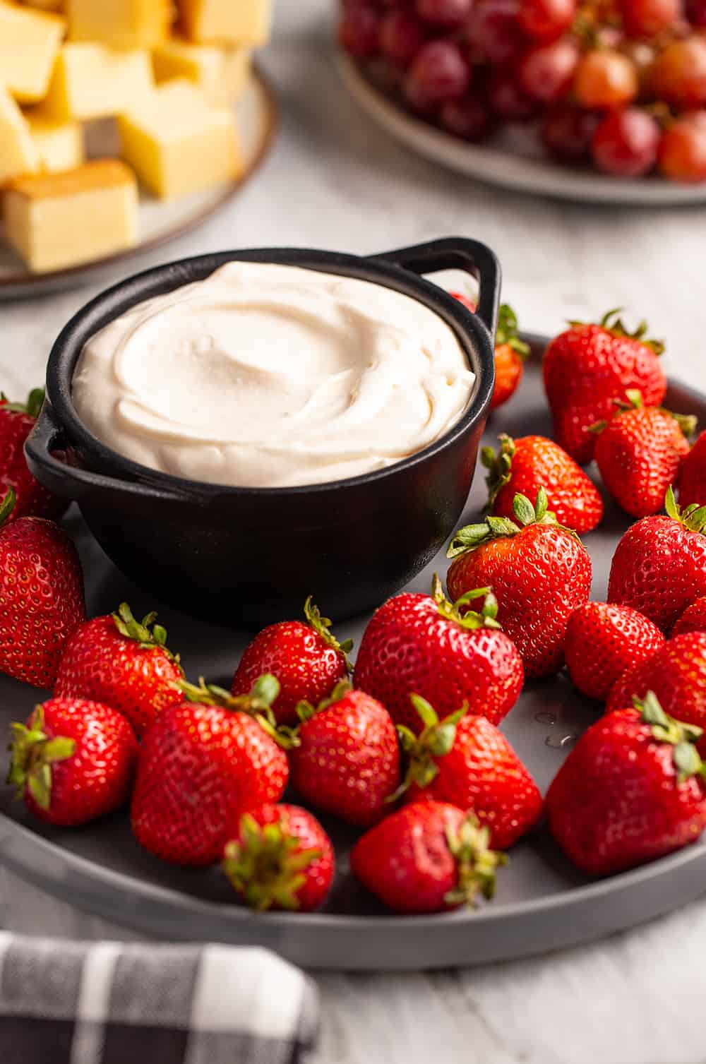 Fruit dip on a serving platter surrounded by strawberries, set on a marble countertop
