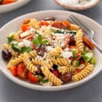 Greek pasta salad with a fork in a white bowl.