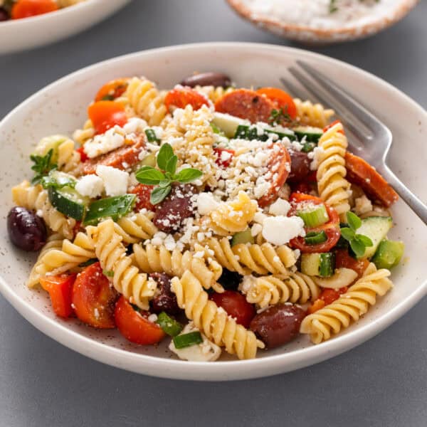 Greek pasta salad with a fork in a white bowl.