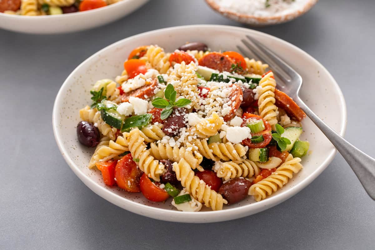 Fork and greek pasta salad in a white bowl.