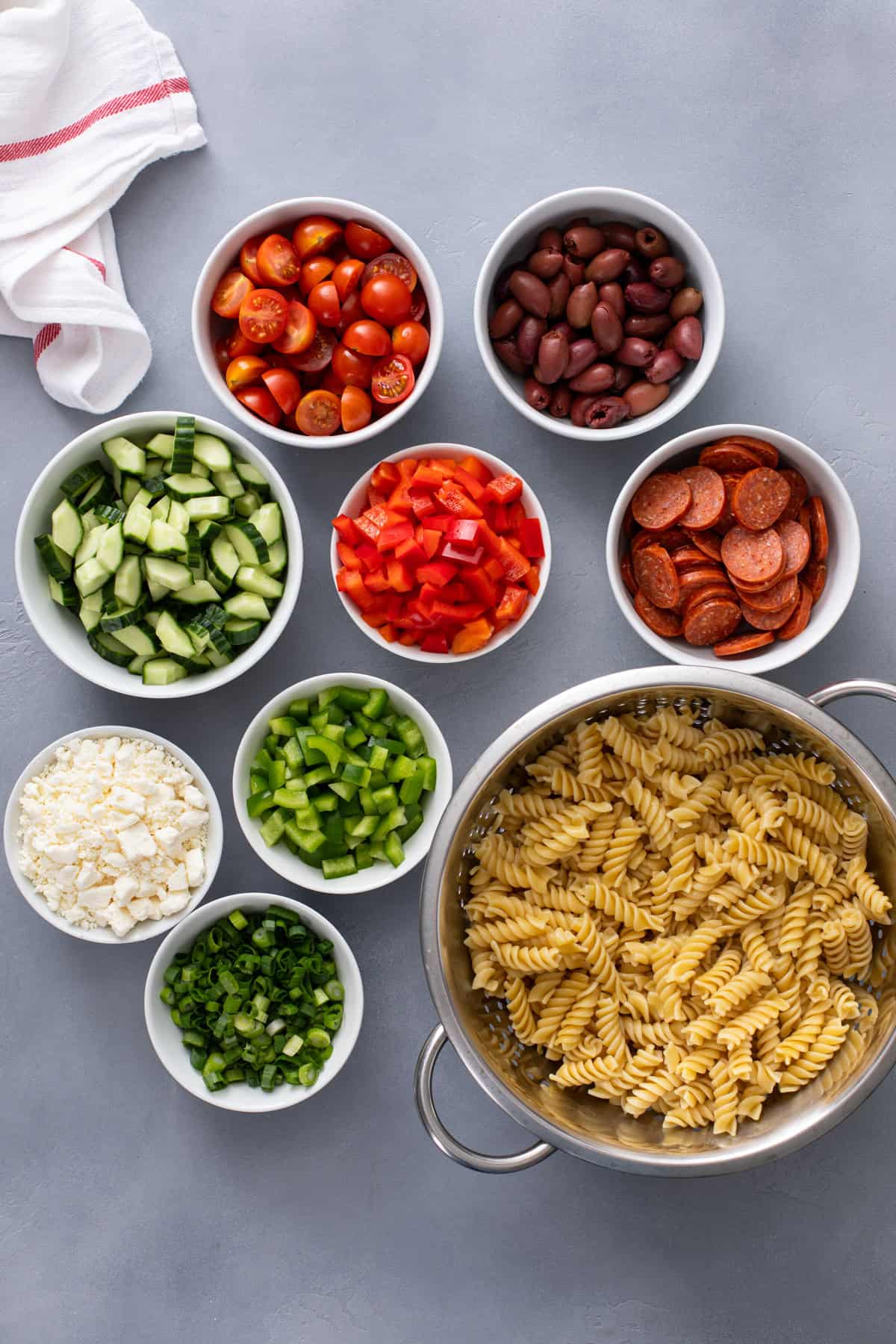Ingredients for greek pasta salad arranged on a countertop.