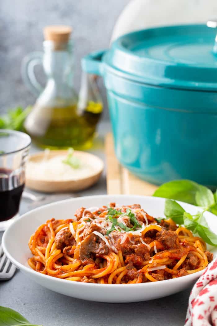 White serving bowl filled with one-pot spaghetti, with the dutch oven and a glass of wine in the background