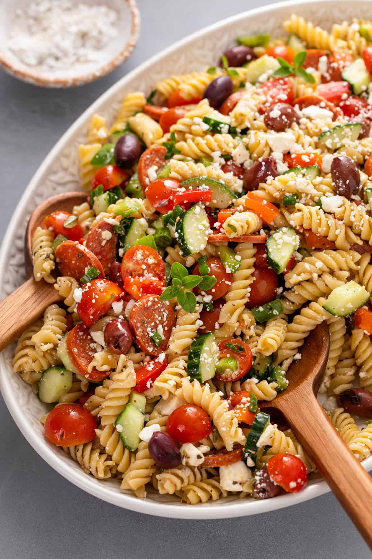 Wooden serving spoons tucked into greek pasta salad in a large serving bowl.