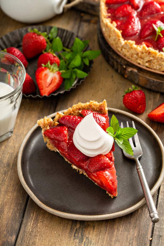 Slice of fresh strawberry pie, topped with a dollop of whipped cream, on a black plate