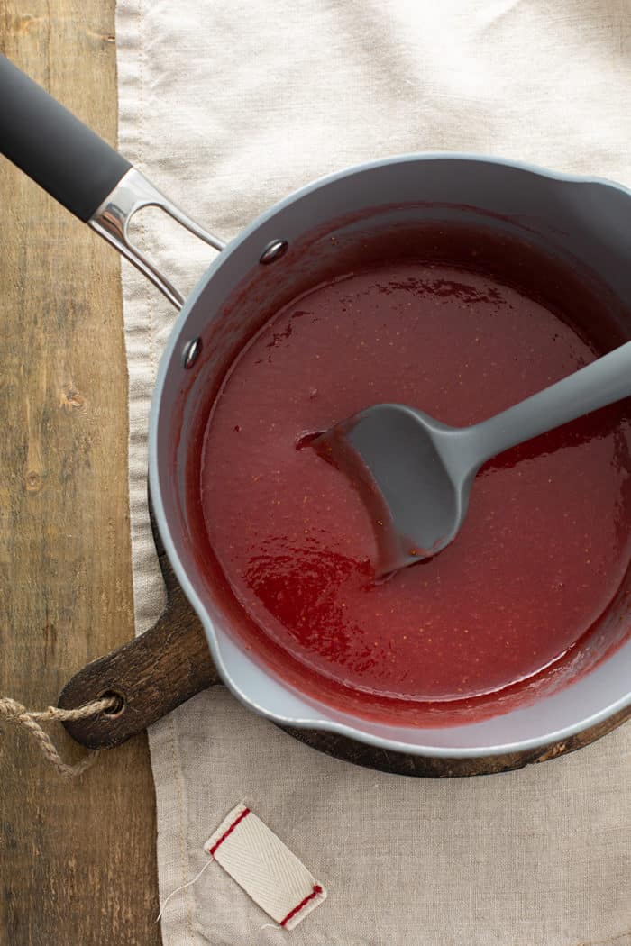 Fresh strawberry pie glaze being stirred by a spatula in a saucepan