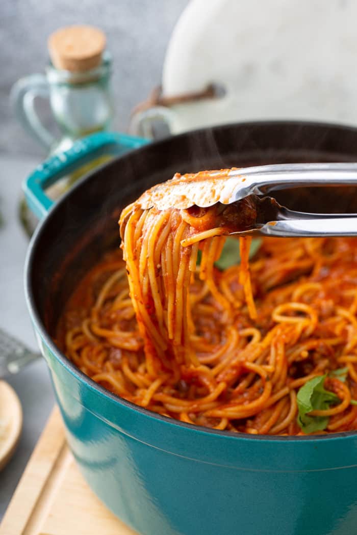 Tongs pulling a serving of one-pot spaghetti out of the pot