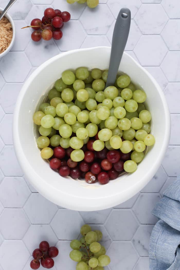 Spatula about to fold red and green grapes into a dressing for creamy grape salad