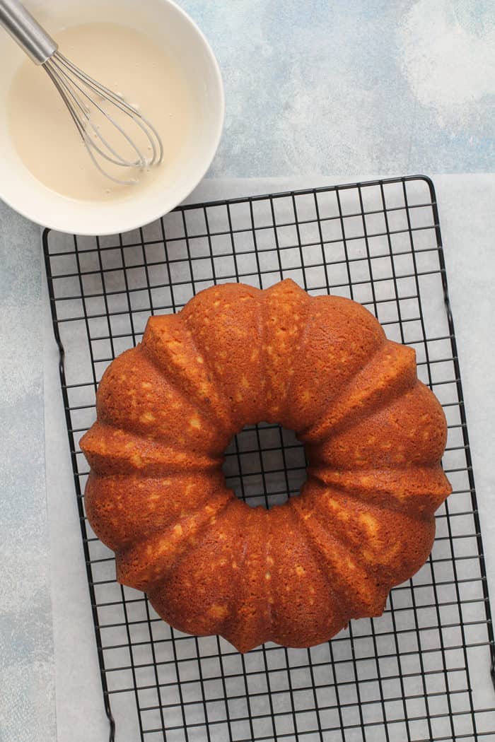 Baked lime coconut cake cooling on a wire rack next to a bowl of glaze