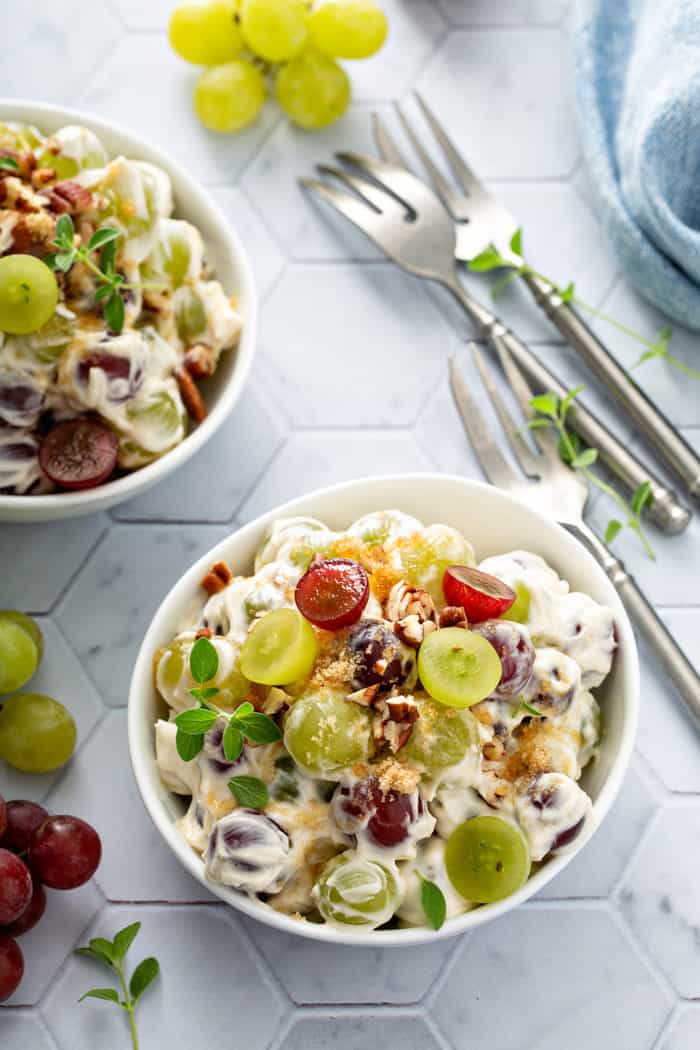 Two small bowls filled with creamy grape salad next to forks on a tiled countertop