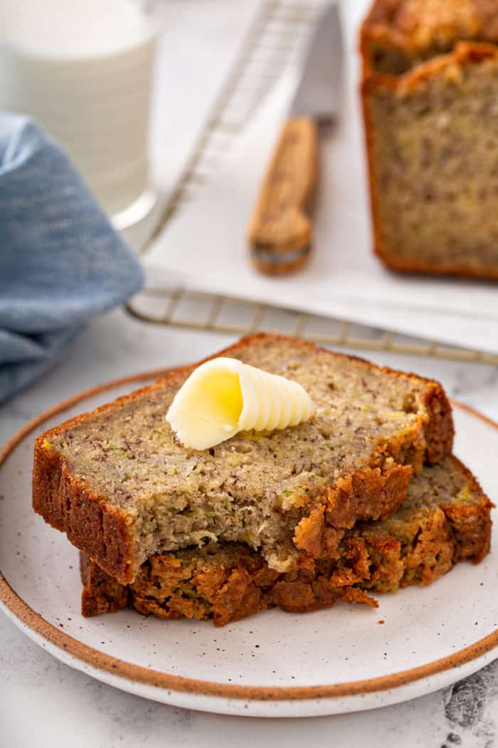 Buttered slice of zucchini banana bread with a bite taken out of it on a plate