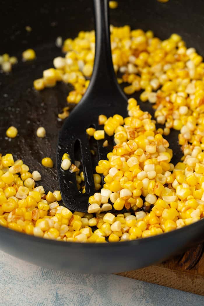 Spatula stirring charred corn in a skillet