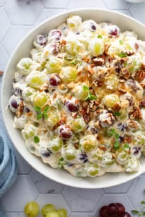 Close up of creamy grape salad in a white serving bowl, topped with toasted pecans
