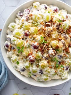 Close up of creamy grape salad in a white serving bowl, topped with toasted pecans