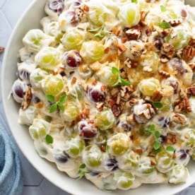 Close up of creamy grape salad in a white serving bowl, topped with toasted pecans