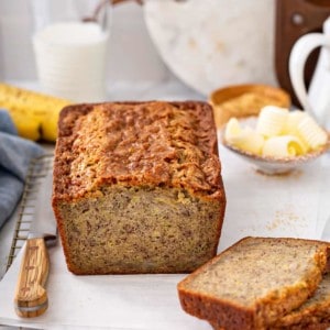 Loaf of zucchini banana bread sliced in half, surrounded by butter and a knife on a countertop