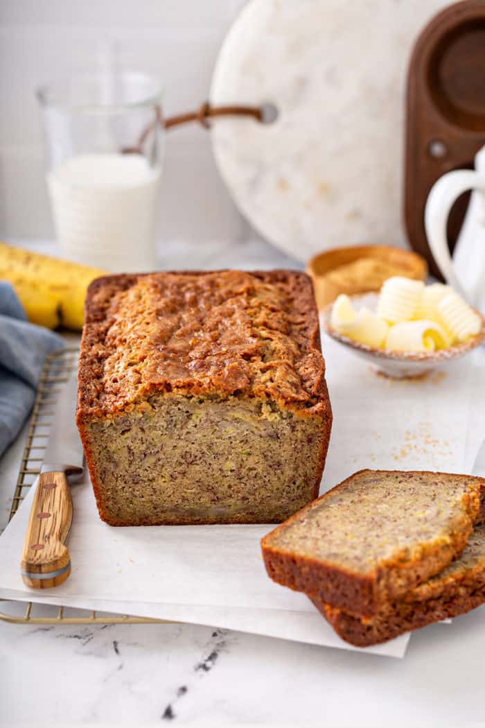 Loaf of zucchini banana bread sliced in half, surrounded by butter and a knife on a countertop