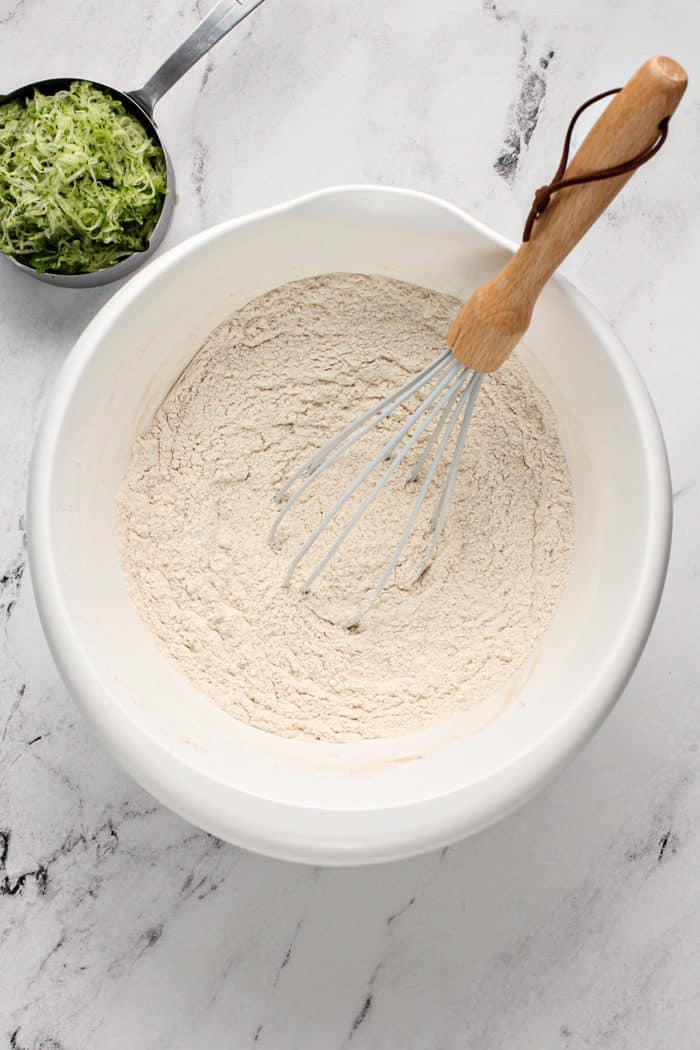 Whisk stirring together the dry ingredients for zucchini banana bread in a white mixing bowl