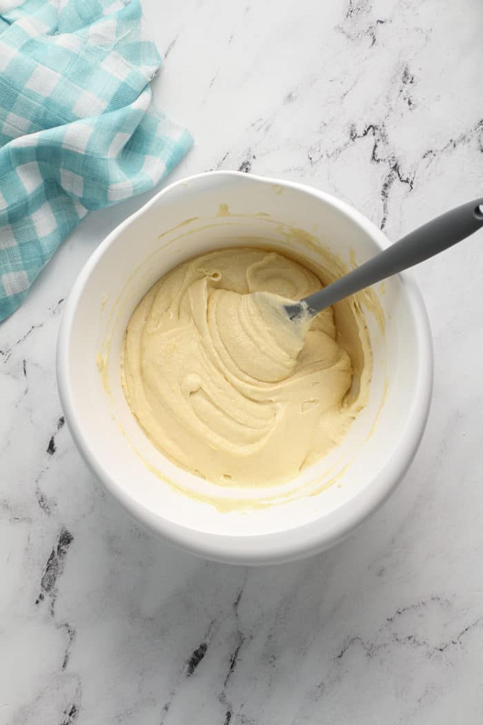 Spatula folding together lemon whipping cream cake batter in a white mixing bowl