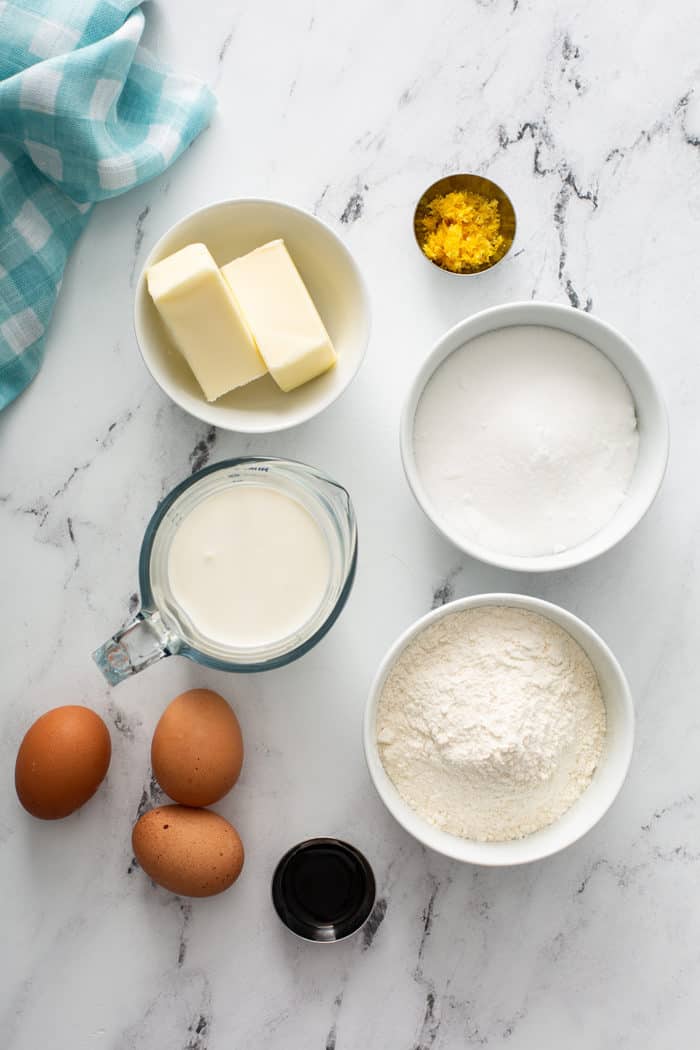 Overhead view of ingredients for lemon whipping cream cake arranged on a marble countertop