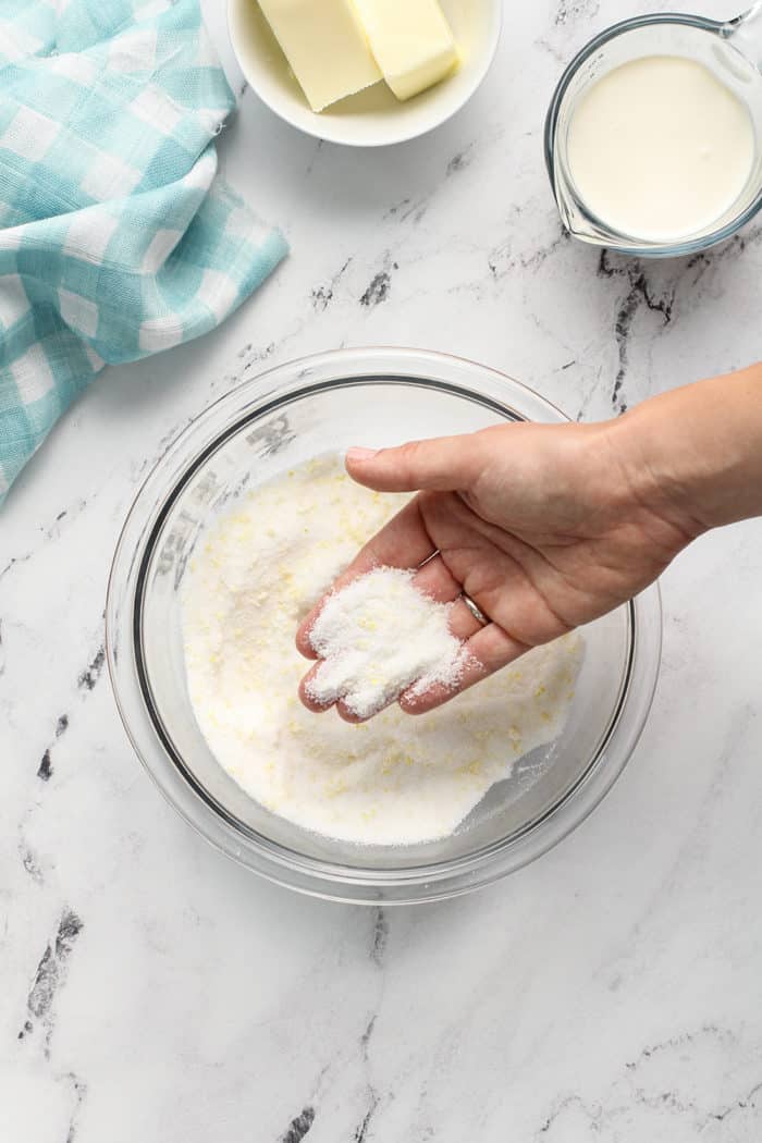 Hand showing sugar and lemon zest rubbed together in a glass mixing bowl