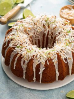 Glazed lime coconut cake on a white cake plate, garnished with lime zest and toasted coconut
