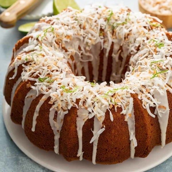 Glazed lime coconut cake on a white cake plate, garnished with lime zest and toasted coconut