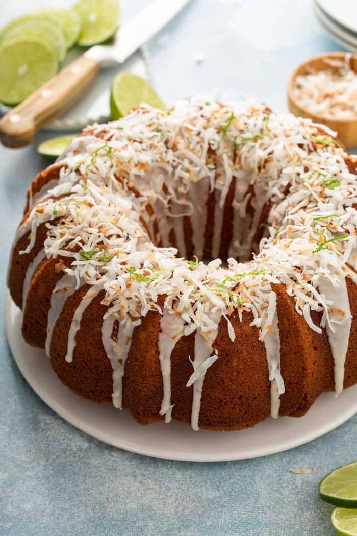 Glazed lime coconut cake on a white cake plate, garnished with lime zest and toasted coconut