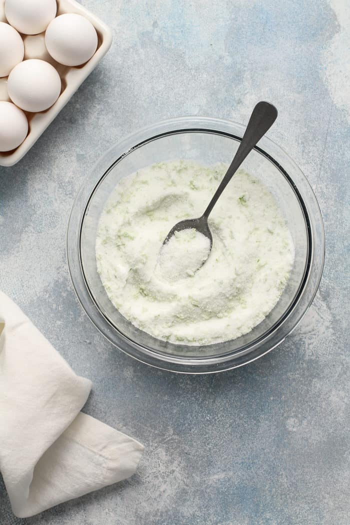 Spoon stirring lime zest combined with granulated sugar in a small glass bowl