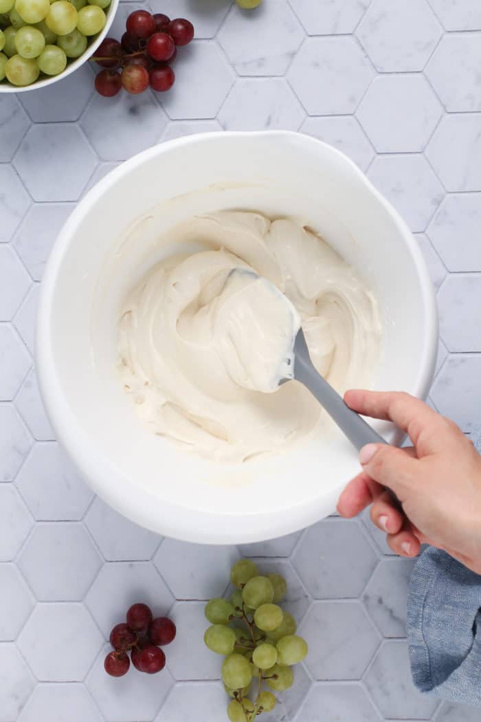 Spatula stirring together the ingredients for the base dressing of creamy grape salad