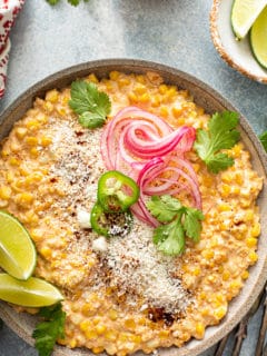 Close up of Mexican street corn salad topped with lime, cotija cheese, cilantro and pickled onions