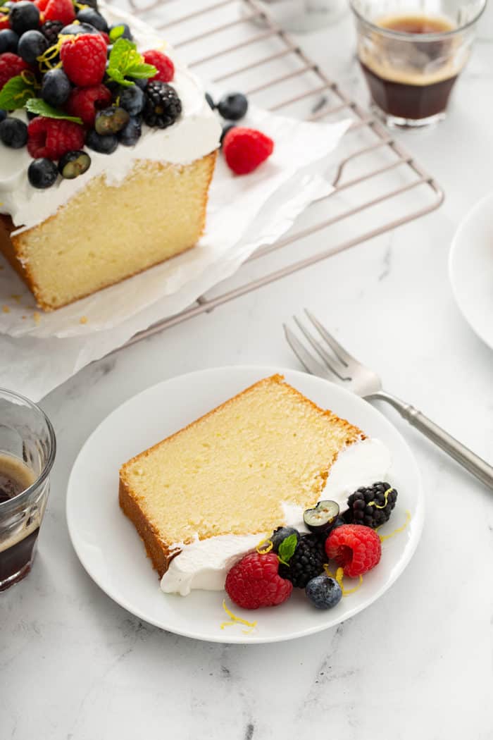 Slice of lemon whipping cream cake on a white plate, with a fork and more cake on the counter next to it