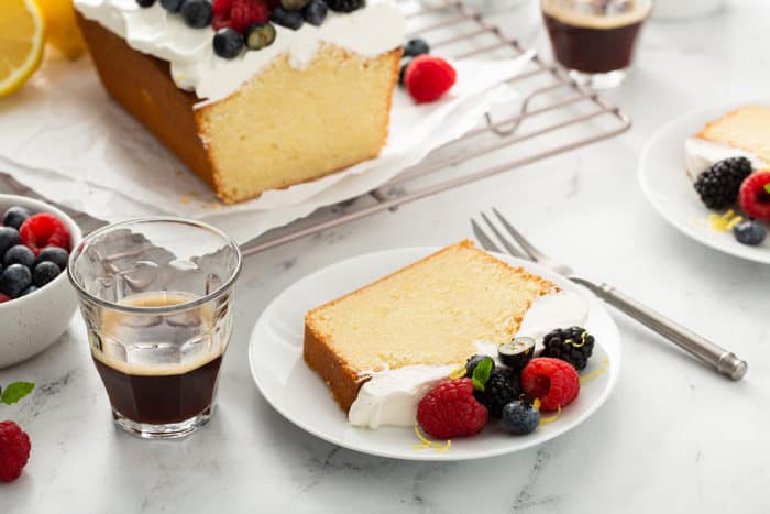 Plates of lemon whipping cream cake next to cups of espresso on a marble counter