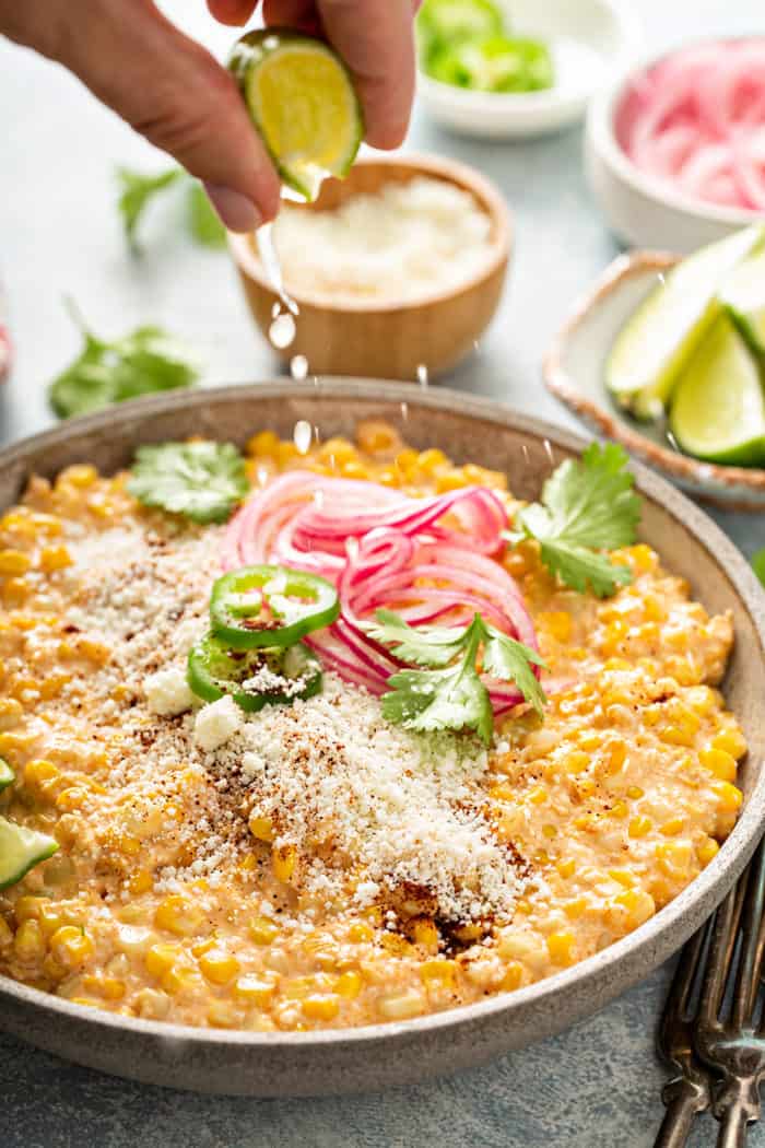 Hand squeezing a wedge of lime over the top of a bowl of Mexican street corn salad