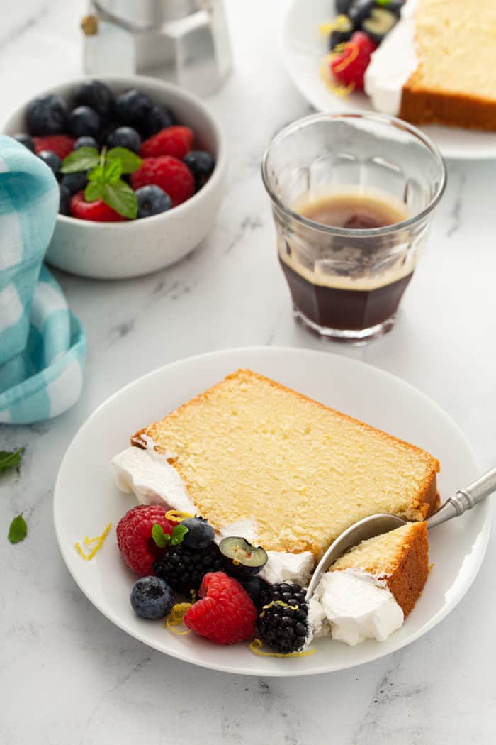 Fork cutting a bite out of a slice of lemon whipping cream cake on a white plate