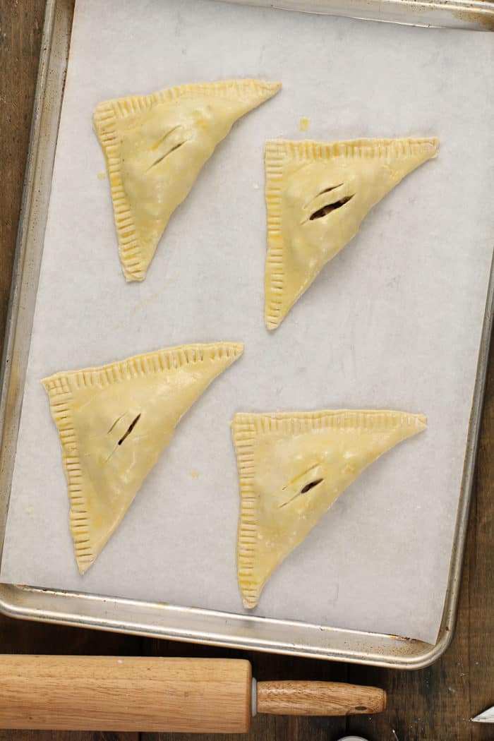 Four unbaked apple turnovers arranged on a baking sheet, ready to bake