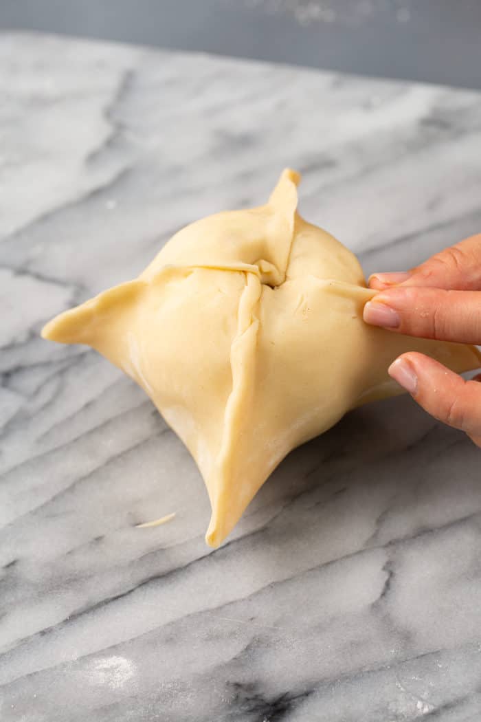 Pie dough wrapped around an apple, set on a marble countertop