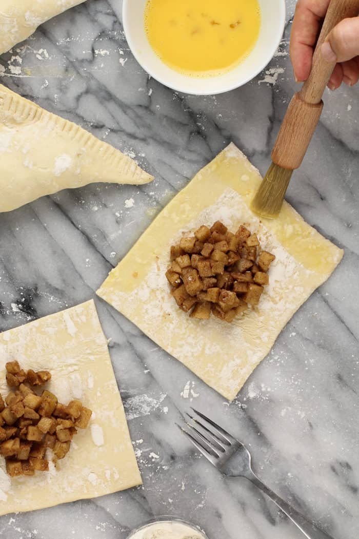 Egg wash being brushed on the edges of apple turnover dough, ready to fold in half